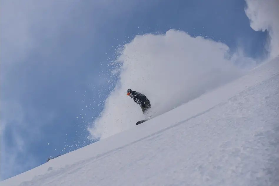 A snowboard comes down the Mammoth Mountain with a large trail of snow behind him